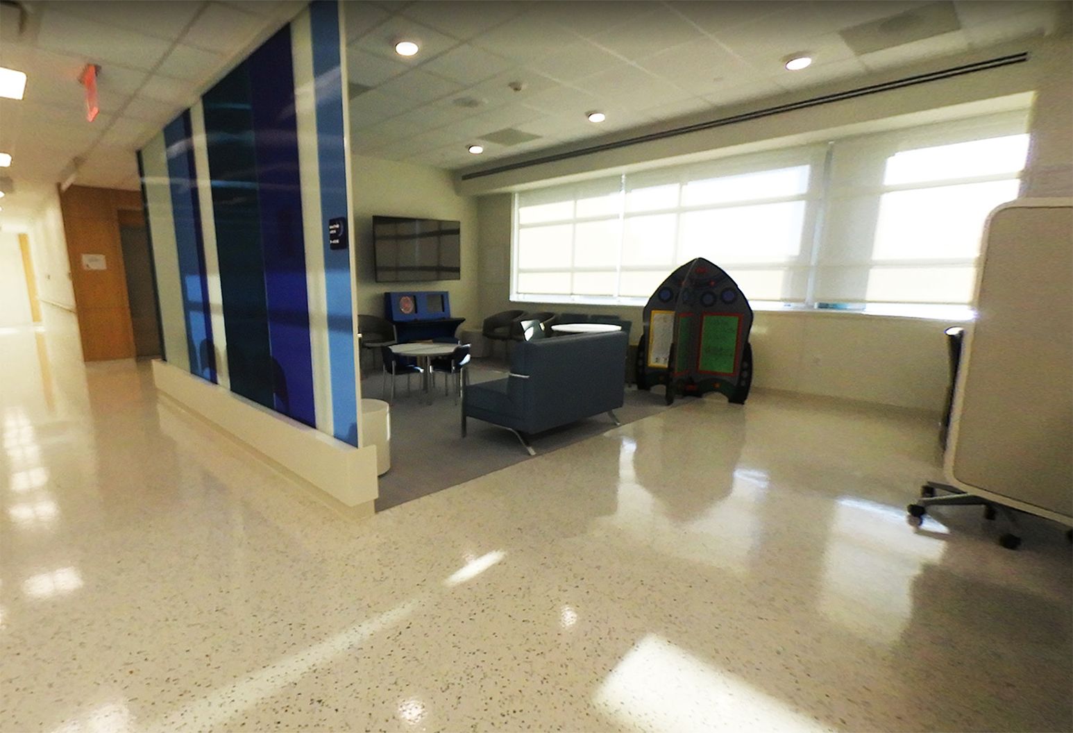 This is the waiting area of our new MRI suite. A modern blue and white divider separates a waiting room filled with couches, tables and a large window from the rest of the facility.